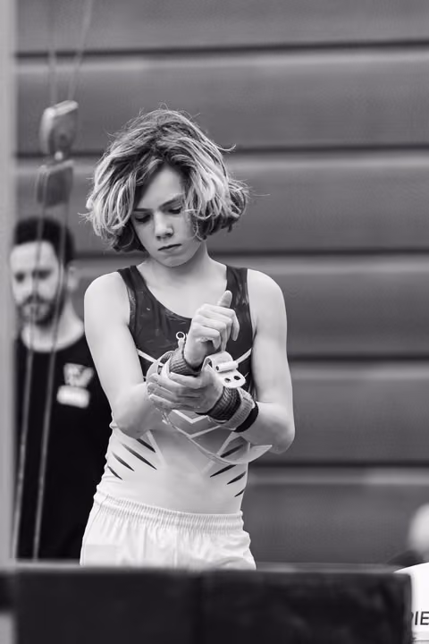 Young female gymnast with short blonde hair concentrates while applying chalk to her hands in preparation for her routine
