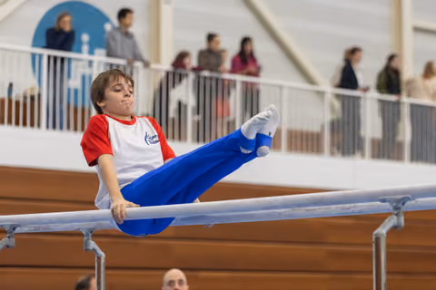 Young gymnast executes a horizontal hold on parallel bars with focused concentration while spectators watch from above