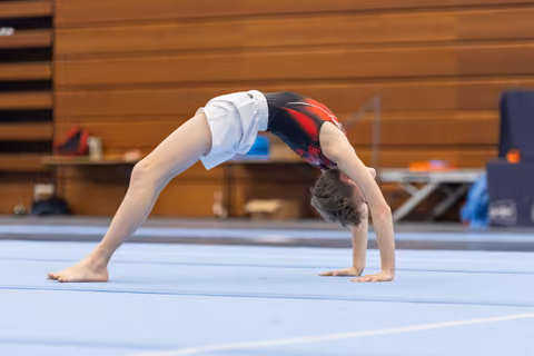 Young gymnast executing a backbend bridge position during floor exercise practice in an indoor training facility