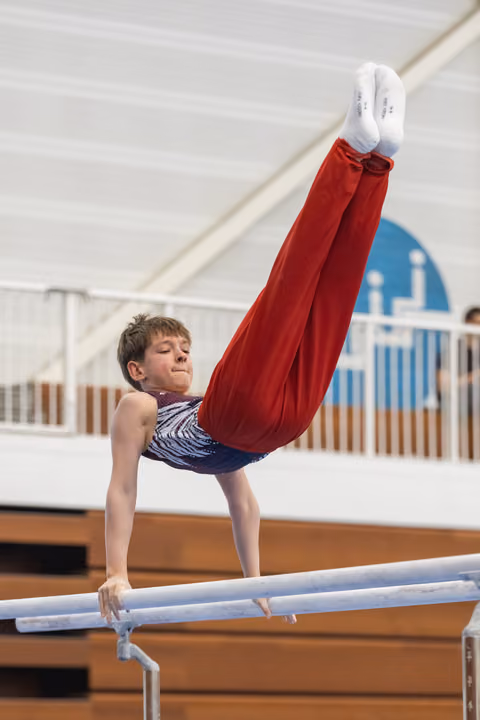Young gymnast performing handstand with legs extended vertically on parallel bars in indoor training facility