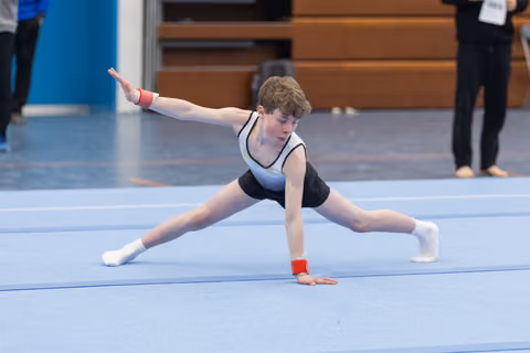 Young gymnast executes a wide split pose with one hand on the floor during a routine, showing strength and flexibility
