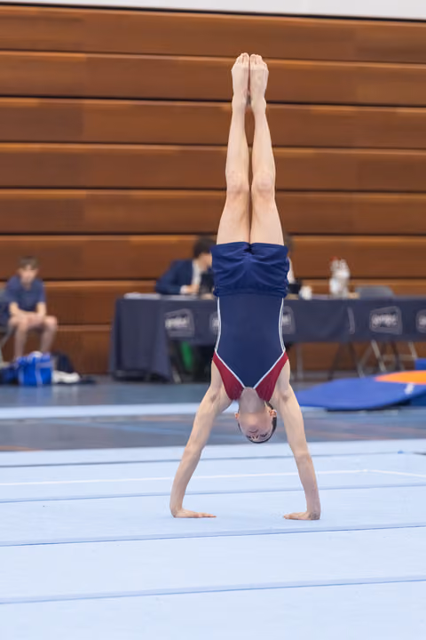 Young gymnast executes a straight handstand on floor exercise mat, demonstrating balance and control during routine