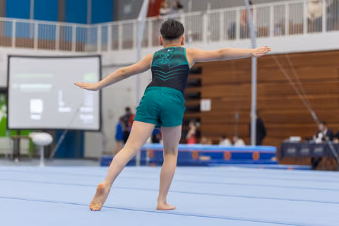 Young gymnast in green uniform performs an elegant pose during floor exercise routine at indoor gymnastics meet