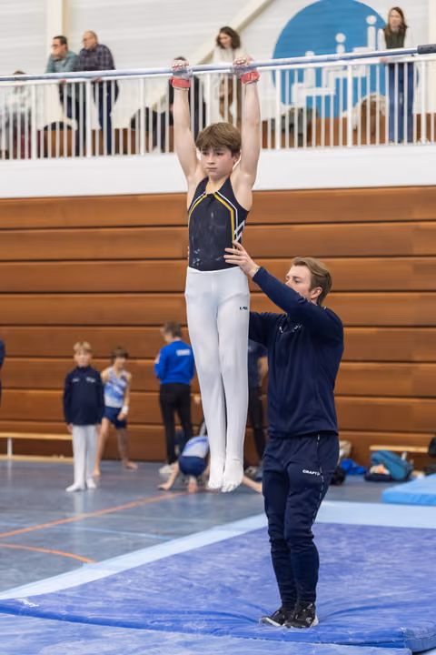 Coach steadies young gymnast performing vertical hold on parallel bars while teammates practice in background