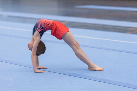 Young gymnast performing a deep backbend bridge on blue floor mat, demonstrating flexibility and strength
