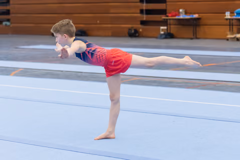 Young gymnast demonstrates horizontal balance pose on floor mat, arms and back leg extended in perfect alignment