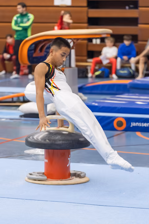 Young male gymnast performing a strength hold on mushroom circle apparatus, legs extended horizontally in competition venue