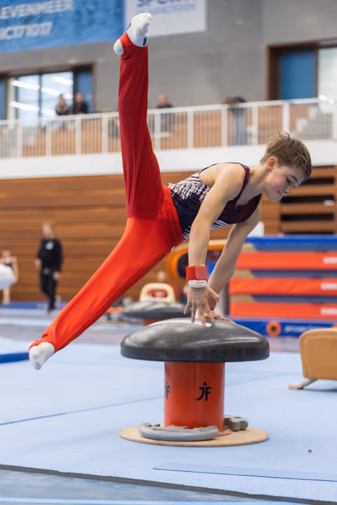 Young gymnast performing a horizontal hold on pommel mushroom, demonstrating strength and control in red tracksuit