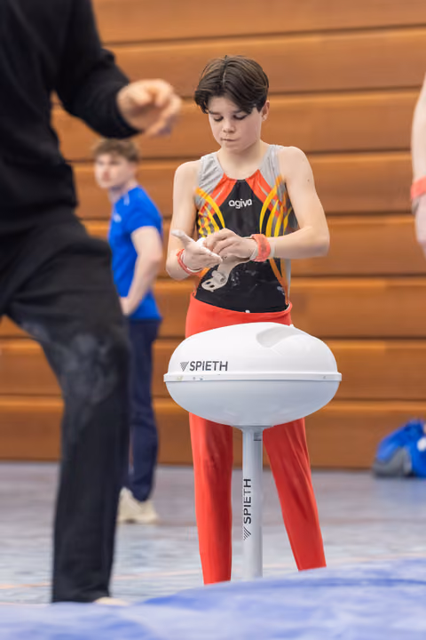 Young gymnast in colorful leotard carefully applies chalk to hands while standing at vaulting table, focused and preparing