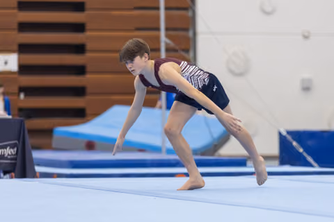 Young gymnast performing floor routine with intense concentration, arms extended in dynamic landing position