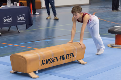 Young gymnast in white and red leotard positions himself at the vault, focused and ready to perform his routine
