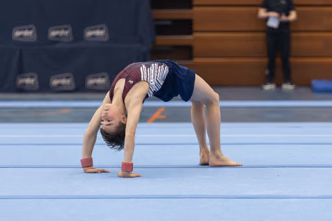 Gymnast performs a backbend bridge on the blue floor mat, displaying flexibility and form during floor exercise routine