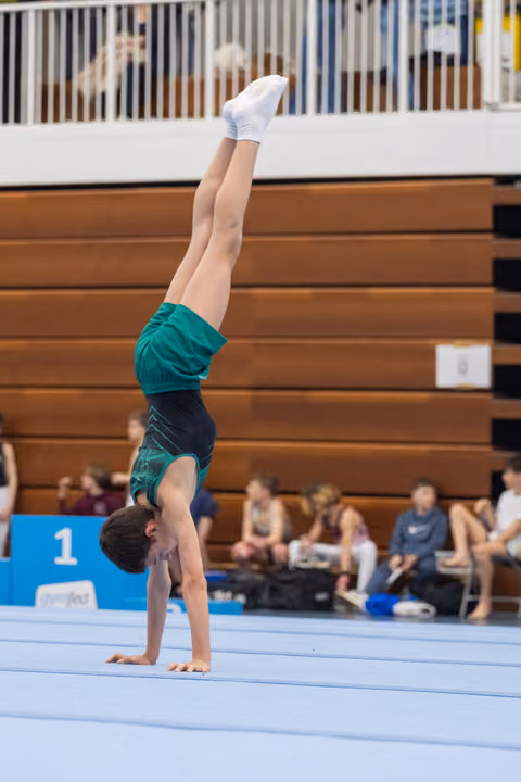 Young gymnast performs a straight handstand on floor exercise mat, demonstrating control and balance during routine