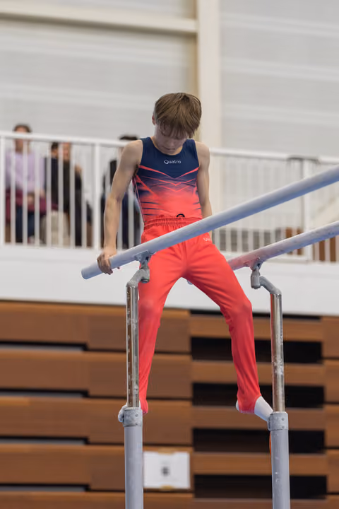Young gymnast in red pants and gradient leotard focuses intently while performing on parallel bars in indoor training facility