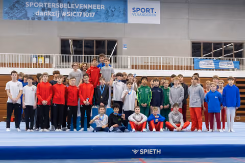 Large group of young gymnasts in team tracksuits pose together with coaches after awards ceremony in indoor sports hall