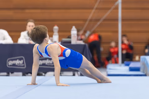 Young gymnast in blue leotard performs plank position on floor mat, demonstrating strength and form during routine