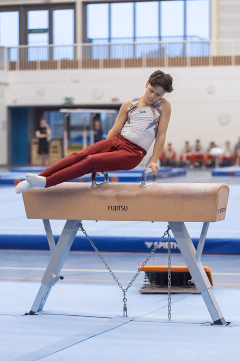 Male gymnast executing a horizontal hold on pommel horse, demonstrating strength and focus during routine at indoor facility