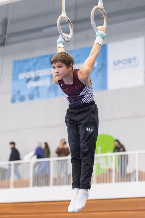 Young gymnast performs on still rings, arms extended overhead, displaying concentration and strength during routine