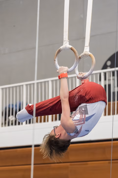 Young gymnast performs inverted position on rings, gripping equipment while upside down in indoor training facility