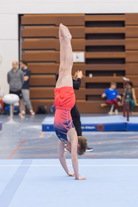 Young gymnast performs a straight handstand on floor exercise mat during training session in gymnasium