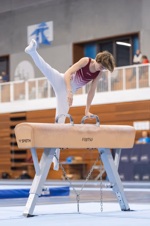 Gymnast performs handstand balance on pommel horse using grips, demonstrating strength and control in training facility