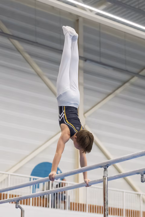 Young gymnast executes a vertical handstand on parallel bars, displaying strength and balance in an indoor training facility