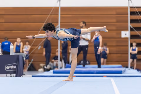 Gymnast executes a graceful arabesque balance on floor, arms extended, demonstrating flexibility and control during routine