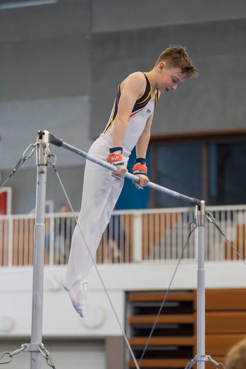 Young male gymnast grips the horizontal bar with intense focus, body horizontal, wearing a black and yellow leotard.