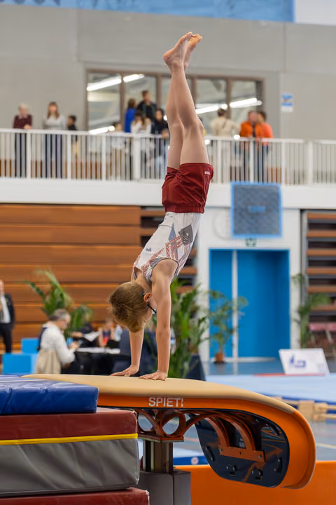 Young gymnast performs a precise handstand on a Spieth vault in an indoor gymnastics hall, body fully extended upward.