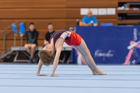 Young gymnast performs a back bridge on the floor, head tilted back, focused during a gymnastics meet.