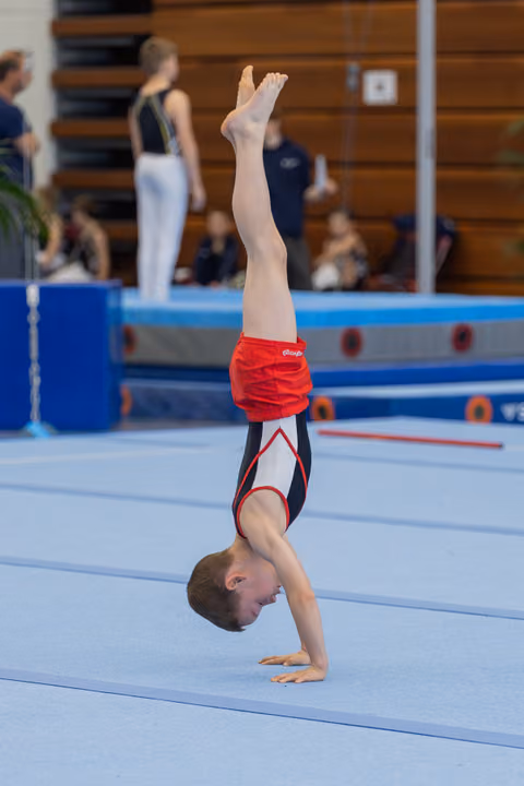 Young boy holds a perfect handstand on the floor mat, focused and controlled, during a gymnastics competition.