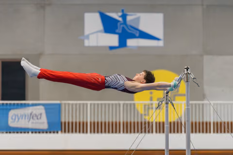 Young male gymnast performs a perfect horizontal iron cross hold on the high bar, body rigid with focused intensity.