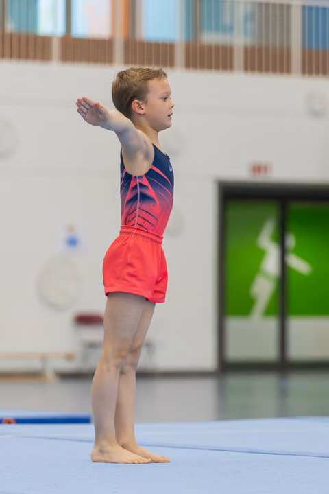 Young male gymnast stands tall on the floor mat, arm raised in a focused salute before his routine begins.