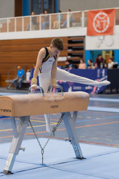 Young male gymnast performs a pommel horse routine, legs extended, with intense focus during an indoor gymnastics meet.