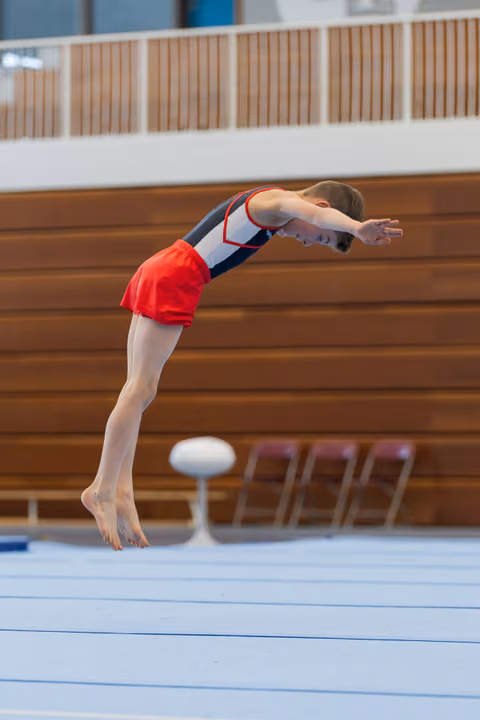 Young gymnast executes a powerful dive roll, body arched and arms extended, mid-air above the floor exercise mat.