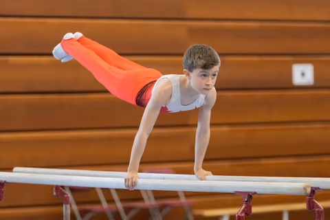 Young male gymnast holds a planche on parallel bars, body horizontal, expression intense and concentrated in a gymnasium.