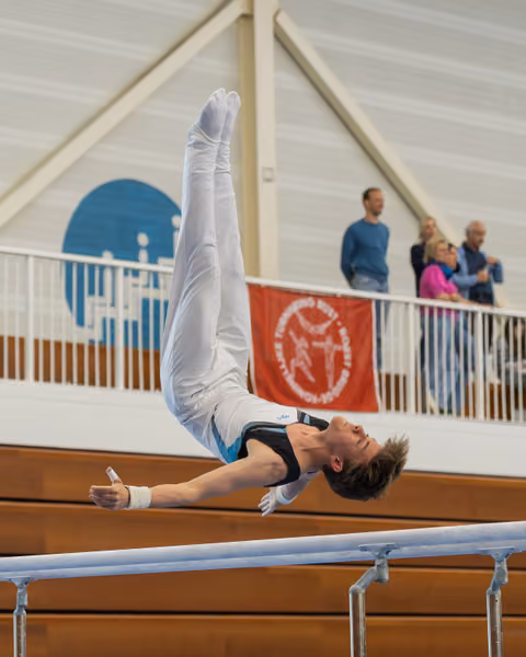 Male gymnast performs a dramatic horizontal hold on parallel bars, body fully extended, intense focus during competition.