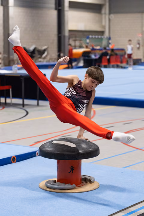 Young gymnast in red pants and sparkly leotard performs a dynamic mushroom circle with legs extended in a training facility