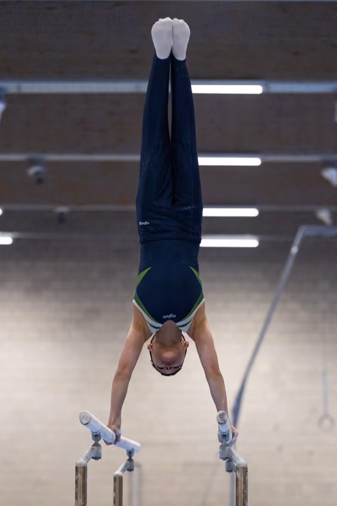 Gymnast executing a vertical handstand on parallel bars, legs straight and pointed, demonstrating balance and control
