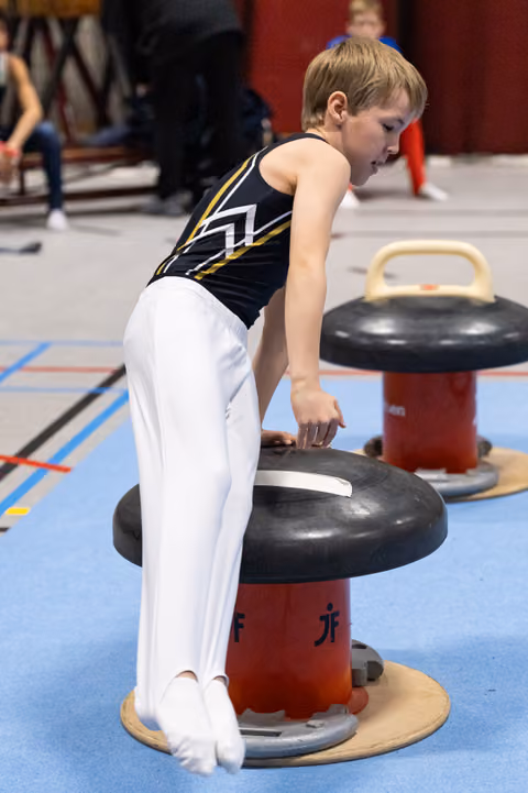 Young gymnast in white and black attire balancing on red mushroom apparatus during training session