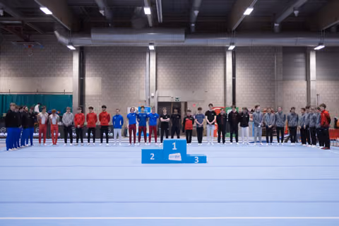 Teams lined up on podium positions at gymnastics venue, athletes in matching team uniforms standing together after awards ceremony