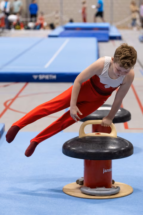 Young gymnast in red and white uniform performs horizontal support position on pommel horse during practice