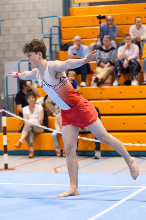 Young gymnast performs an artistic arabesque pose during floor routine, displaying focus and balance before spectators