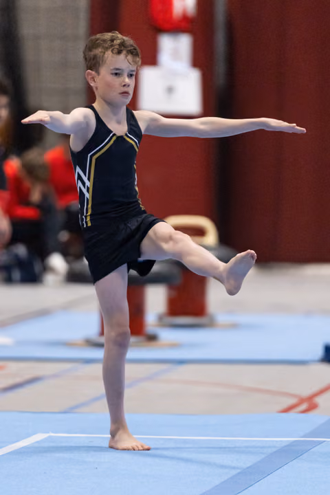 Young gymnast holds a one-legged balance with arms extended during floor routine, displaying focus and poise