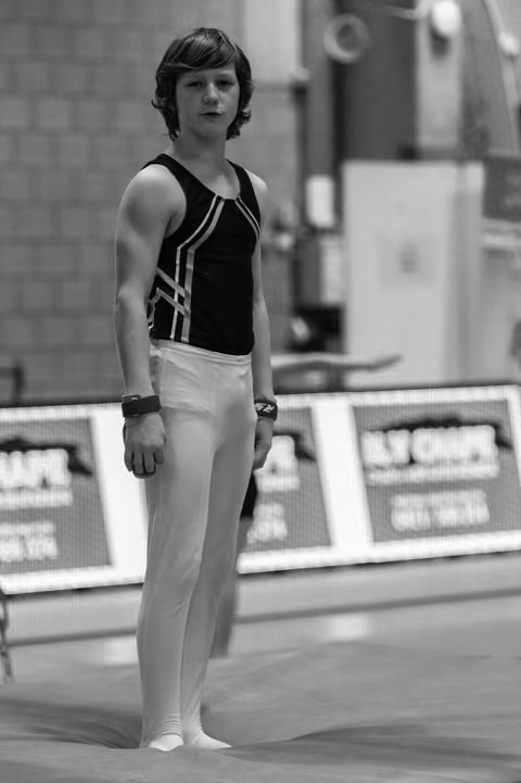 Young male gymnast stands at attention in black and white uniform, focused and composed before his routine