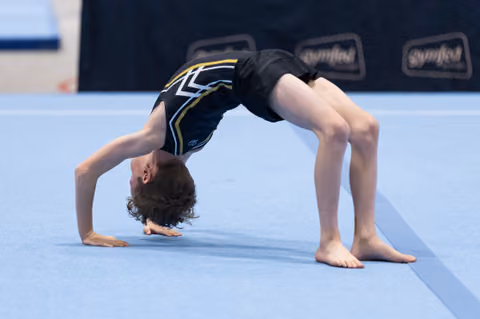 Young gymnast performs a backbend during floor routine, displaying impressive flexibility on blue mat