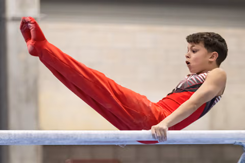 Young gymnast performs a pike position on parallel bars, legs extended upward, displaying strength and concentration