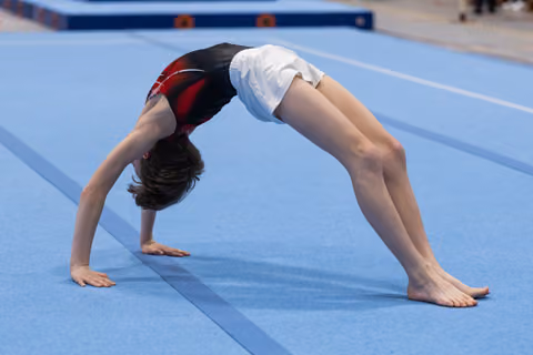 Young gymnast executing a bridge pose on blue mat, demonstrating flexibility with arched back and straight legs