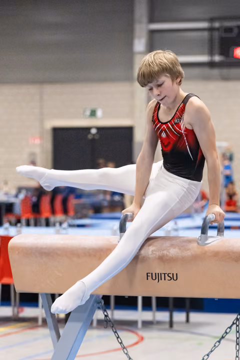 Young gymnast performing circles on Fujitsu pommel horse, displaying intense concentration in white pants and red-black leotard