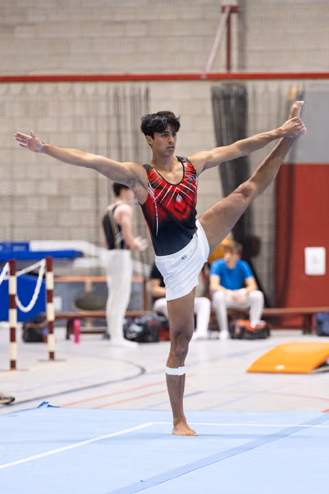 Male gymnast performs an elegant standing leg extension with arms spread wide during floor exercise in training facility